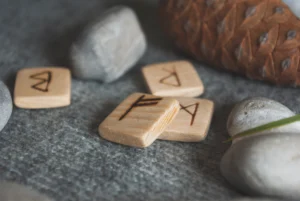 Small wooden rune tiles lay on a grey mat surrounded by natural objects like rocks and pinecones.